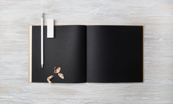 Blank black booklet, pencil and eraser on light wooden background. Branding mock up. Flat lay.