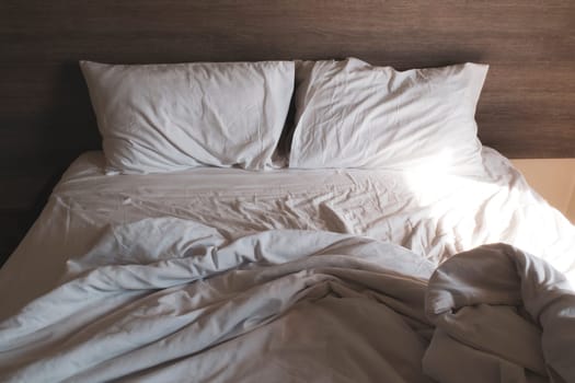 messy comfy white bed sheets and pillow life on Holiday . untidy unmade bed with white crumpled bed sheet and two messy pillows in a hotel room. Holiday weekend Sunday background for relaxation