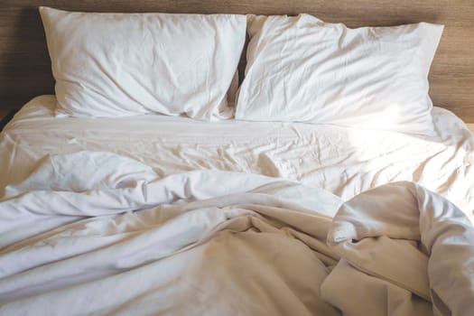 messy comfy white bed sheets and pillow life on Holiday . untidy unmade bed with white crumpled bed sheet and two messy pillows in a hotel room. Holiday weekend Sunday background for relaxation