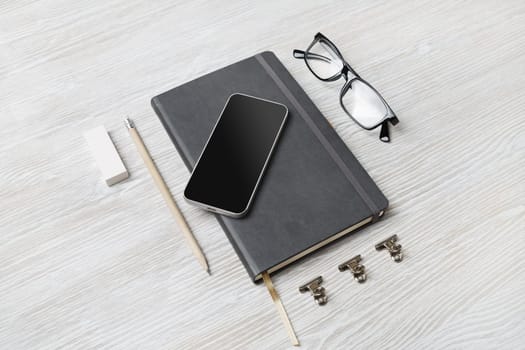 Blank branding stationery set. Blank notepad, smartphone, glasses, pencil and eraser on light wooden background.