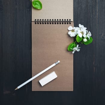Blank kraft notepad, pencil, eraser and spring flowers on wood table background. Top view. Flat lay.