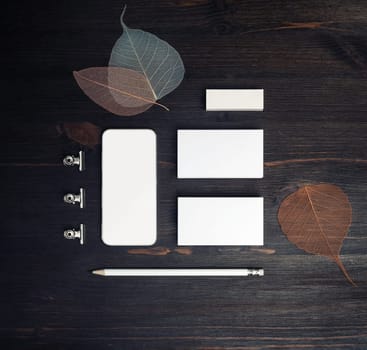 Blank stationery template on wood table background. Business cards, smartphone, pencil, eraser and leaves. Top view. Flat lay.