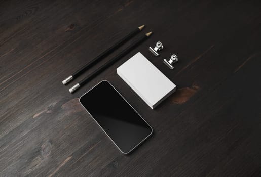 Blank stationery template on wooden background. Smartphone, business cards, pencils and paper clips.