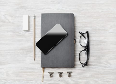 Blank business stationery set. Notebook, smartphone, glasses, pencil and eraser on light wood table background. Flat lay.
