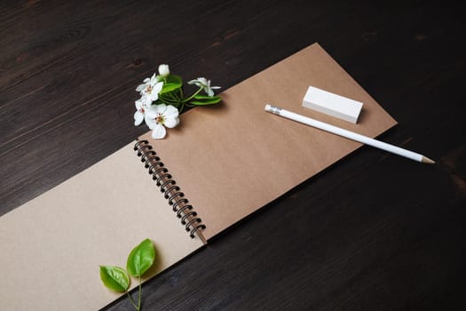 Stationery and flowers. Blank kraft sketchbook, pencil, eraser and spring flowers on wooden background.