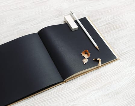 Black brochure, pencil and eraser on light wooden background.