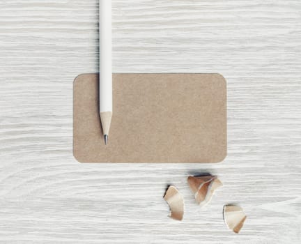 Photo of blank kraft business card and pencil on light wood table background. Blank stationery template. Top view. Flat lay.