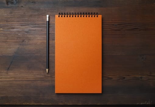 Blank orange notebook and pencil on wooden background. Stationery mock up. Flat lay.