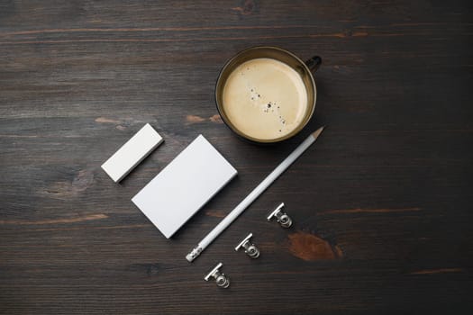 Blank stationery template. Coffee cup, blank business card, pencil and eraser on wooden background. Flat lay.