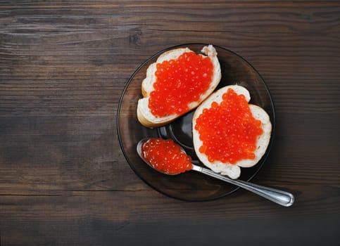 Delicious fresh red caviar, sandwiches, plate and spoon on wood table background. Top view. Flat lay.