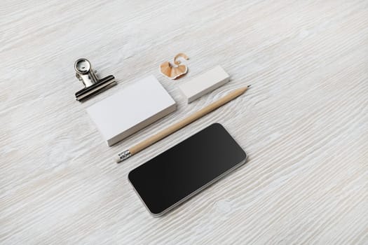Blank branding mockup. Blank business cards, smartphone, pencil and eraser on light wood table background.