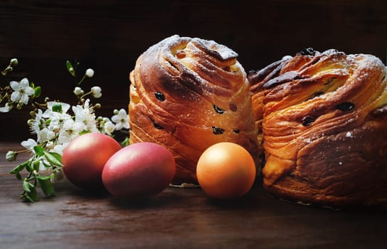 Easter eggs, sweet buns and spring flowers on wooden background.