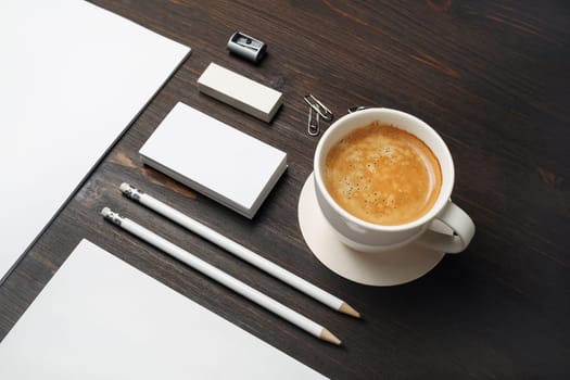 Photo of coffee cup and blank stationery set on wooden background.