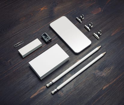 Photo of blank smartphone, business cards, pencils, eraser and sharpener on wood table background. Stationery mock up.