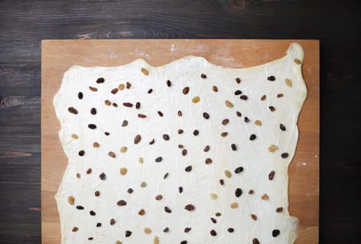 Rolled dough with raisins on wooden cutting board. Top view. Flat lay.