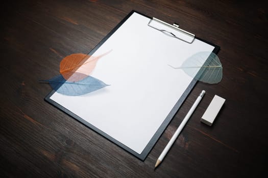 Blank stationery template. Clipboard with blank letterhead, pencil, eraser and leaves on wood table background.