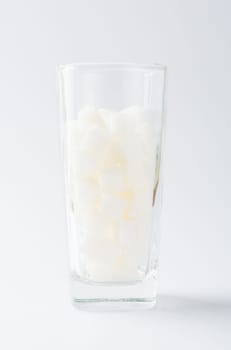 A glass full of white sugar cube sweet food ingredient, studio shot isolated on white background, health high blood risk of diabetes and calorie intake concept and unhealthy drink
