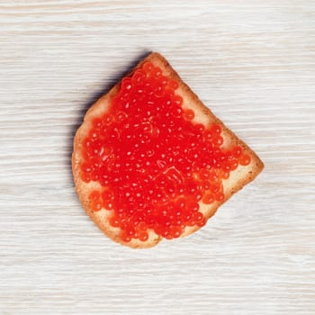 Photo of sandwich with red caviar on light wooden background. Flat lay.