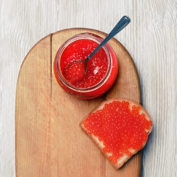 Fresh delicious caviar. Sandwich with red caviar, glass jar and spoon. Flat lay.