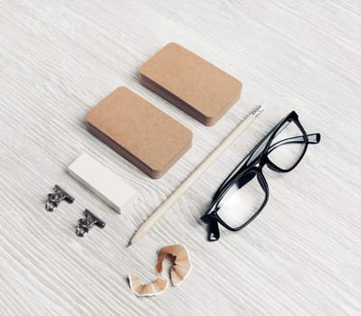 Corporate identity template. Blank kraft business cards, glasses, pencil and eraser on light wood table background.