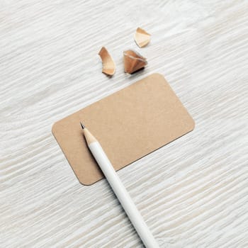 Photo of blank vintage business card and pencil on light wooden background. Mockup for ID.