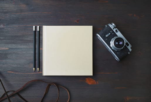 Blank stationery: book, pencils and retro camera on wood table background. Flat lay.