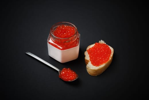 Delicious fresh red caviar. Sandwich with red caviar, glass jar and spoon.