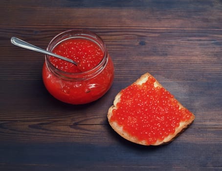Sandwich with red caviar, glass jar and spoon on vintage wood table background. Still life with red caviar.