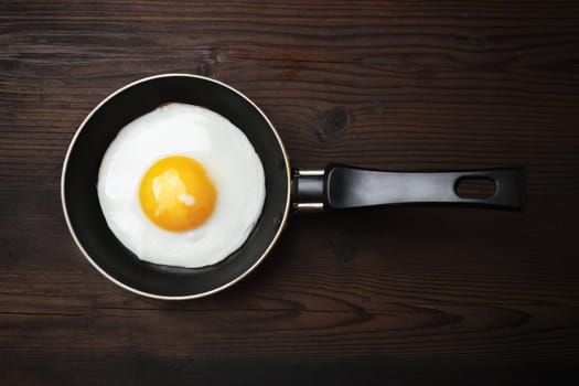 Fried egg in frying pan on wooden background. Flat lay.