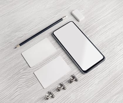 Smartphone, blank business cards, pencil and eraser on light wood table background. Branding identity mock up.