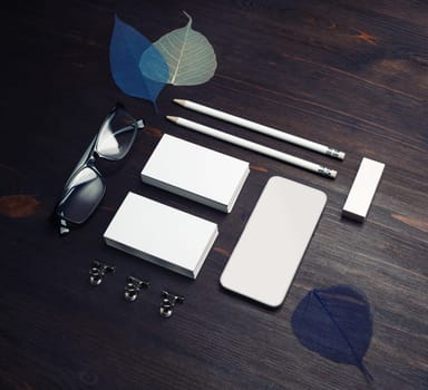 Photo of blank business cards, smartphone, pencils, eraser, glasses and skeletons of leaves on wood table background. Branding mock up.
