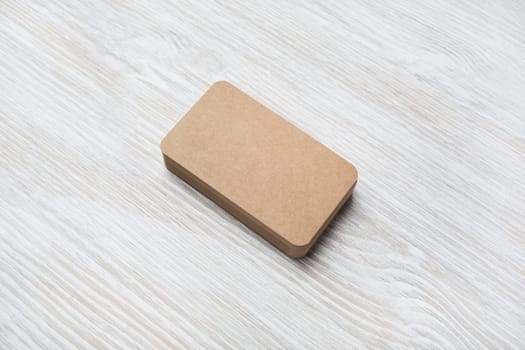 Photo of blank kraft business card on light wood table background. Mock-up for branding identity.