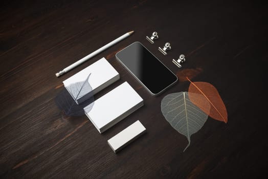 Blank stationery template. Blank business cards, smartphone, pencil, eraser and skeletons of leaves on wooden background.