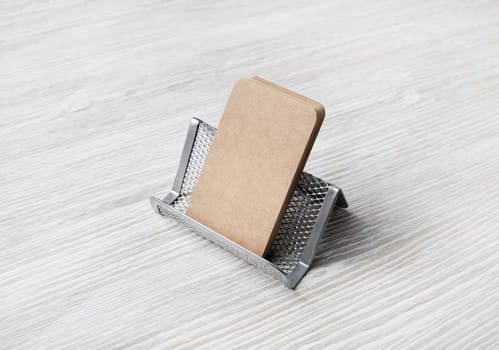 Card holder with blank kraft business cards on light wood table background.