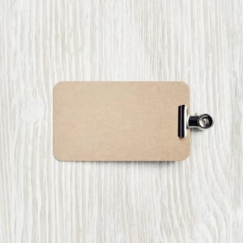 Blank kraft business card and clip on light wooden background. Flat lay.
