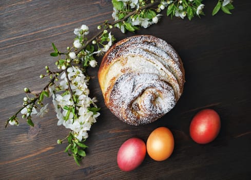 Easter still life. Delicious sweet bun, easter eggs and spring flowers on wood table background. Flat lay.