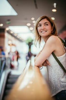 Young girl is leaning on the handrail in a shopping mall, blurry background