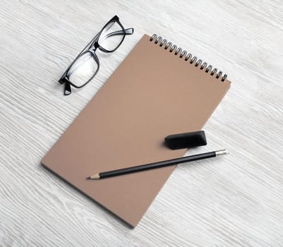 Mockup of vintage stationery. Blank kraft notepad, pencil eraser and glasses on light wooden background. Template for placing your design.
