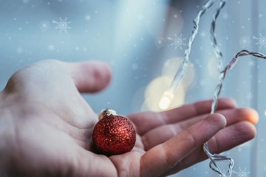 Hand holding a small red christmas bauble, shiny background