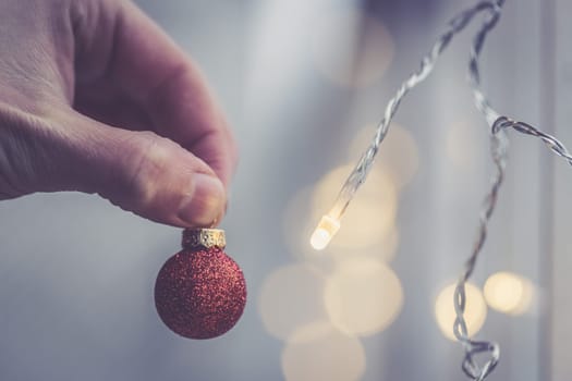 Hand holding a small red christmas bauble, shiny background