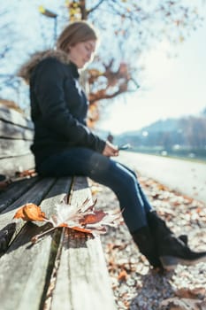 Park bench in autumn, woman sitting on it in the blurry background
