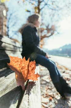Park bench in autumn, woman sitting on it in the blurry background