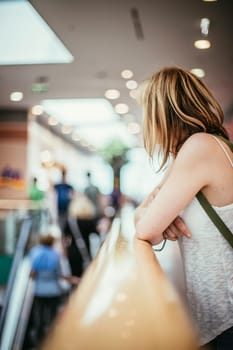 Young girl is leaning on the handrail in a shopping mall, blurry background