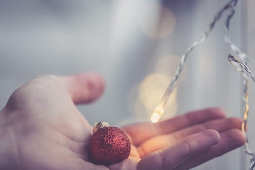 Hand holding a small red christmas bauble, shiny background