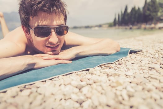 Young handsome man is lying on the beach, sun glasses