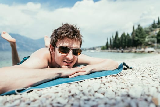 Young handsome man is lying on the beach, sun glasses