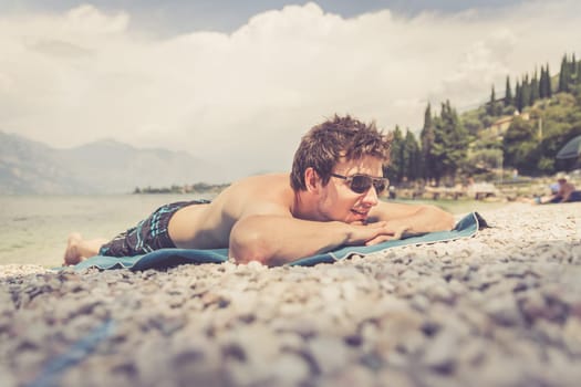 Young handsome man is lying on the beach, sun glasses