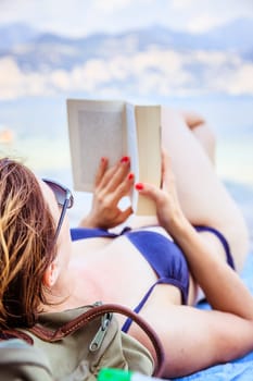 Young beautiful woman in bikini reading a book on the beach