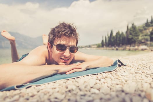 Young handsome man is lying on the beach, sun glasses