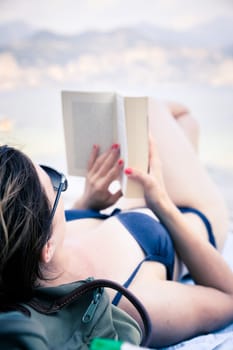 Young beautiful woman in bikini reading a book on the beach